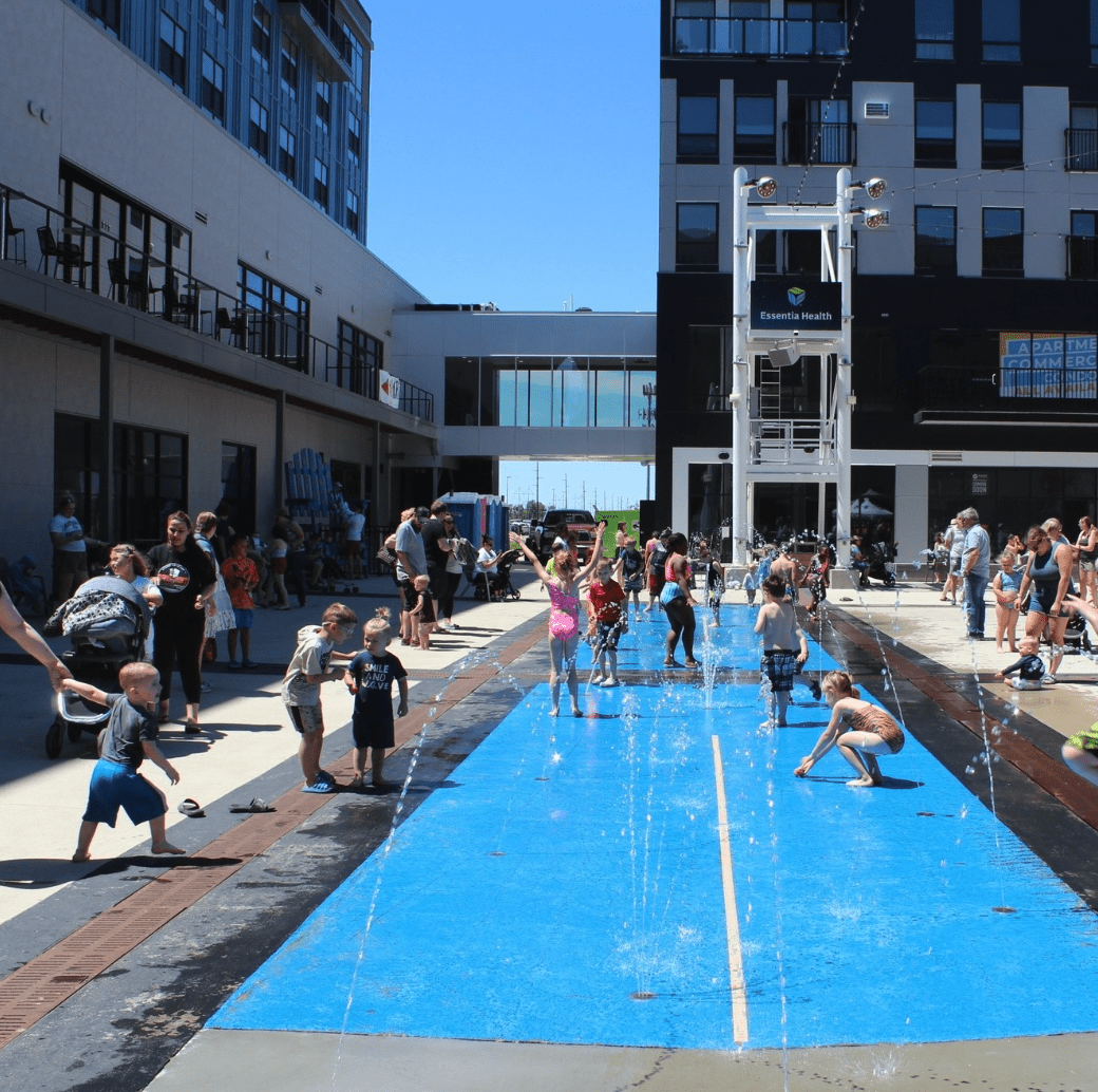 Kids and adults enjoying an outdoor water fountain area in a West Fargo Events plaza